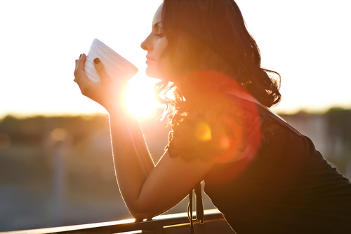 A woman peering into a cup during a sunset.